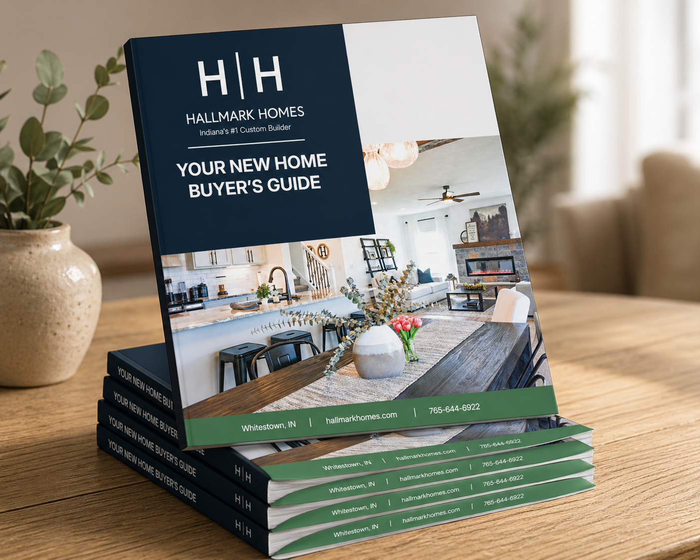 Brochure on a wooden table titled 'Your New Home Buyer’s Guide' by Hallmark Homes, with stacked copies beneath it and a plant nearby.