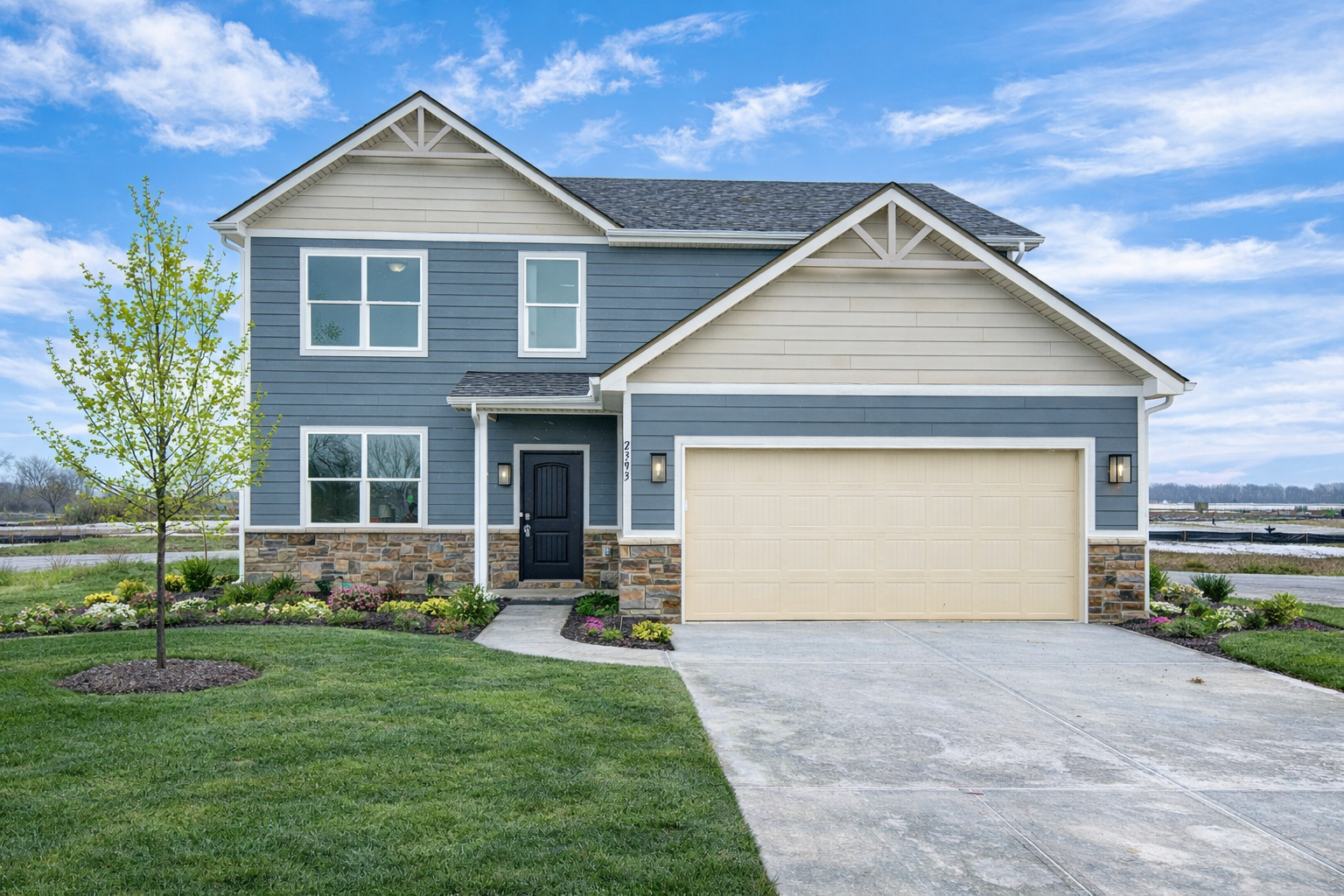Two-story blue house with a beige garage door, stone accents, and a small front garden under a blue sky.